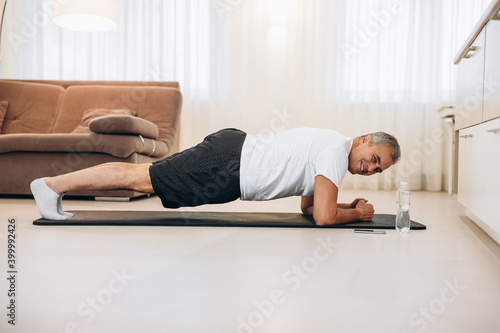 Plank it Confident senior man doing plank position while exercising on the floor in light loft interior. Hard workout. Training at home. Man training to have fit body. Morning workout.