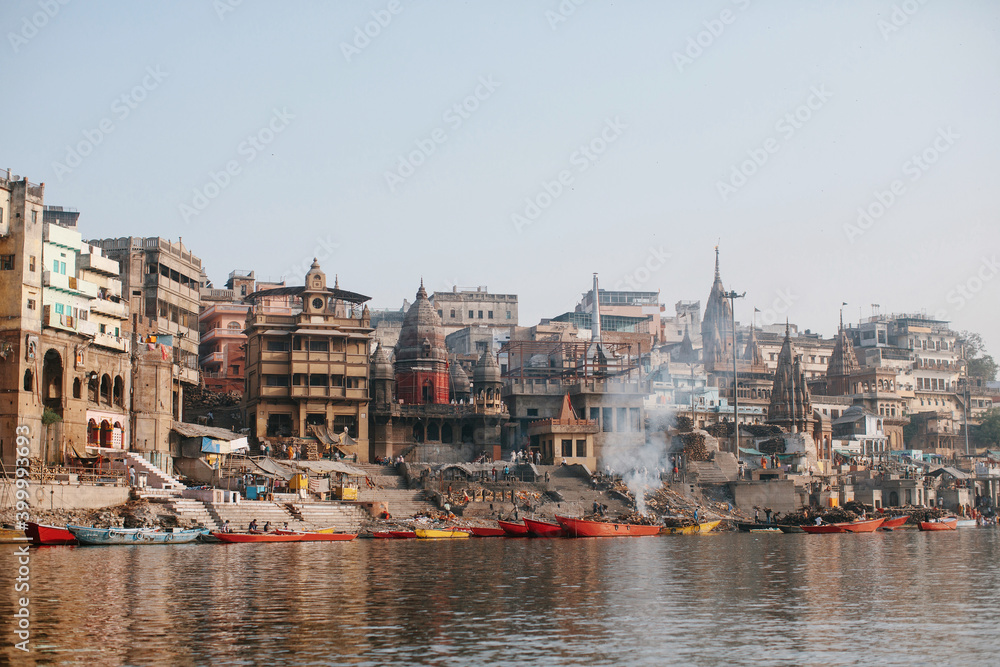Ganga river and Varanasi ghats morning view with buildings, boats and people. Smoke from bonfires