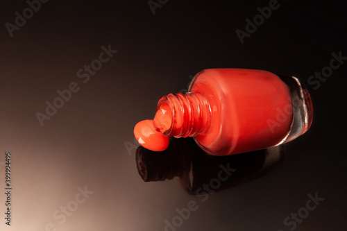 Side view of one red bottle of nail polish with reflections on mirrored surface against dark background