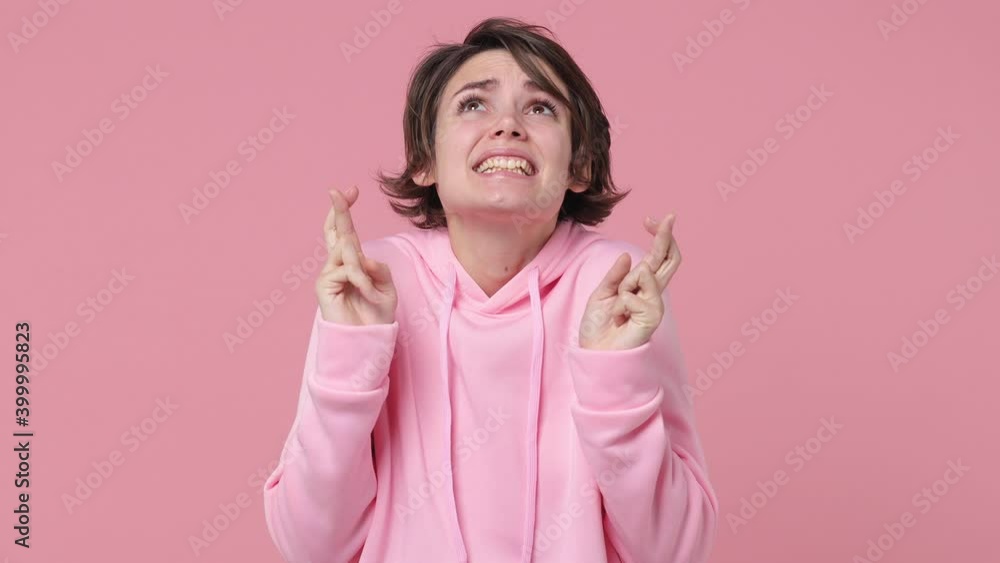 Pleading young woman 20s in streetwear hoodie posing isolated on pastel pink background studio. People lifestyle concept. Wait for special moment keep fingers crossed hands prayer making wish begging Pleading young woman 20s in streetwear hoodie posing isolated on pastel pink background studio. People lifestyle concept. Wait for special moment keep fingers crossed hands prayer making wish begging