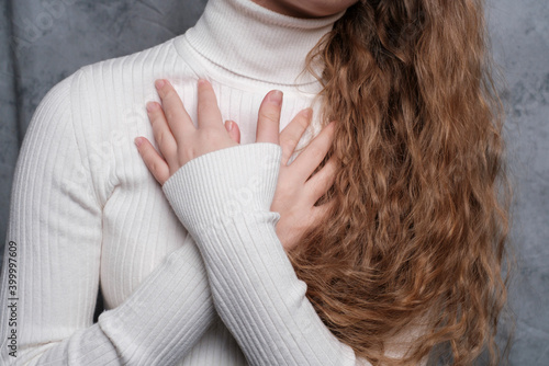 A young woman holds her breasts with her hands. Close-up. Long curly hair, white sweater. Concept of emotional experiences.