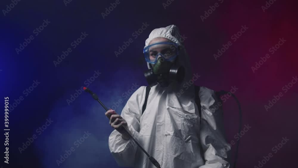 A person in white protective medicine suit standing in smoky room holding cleaning equipment and looking in the camera - red and blue lighting A person in white protective medicine suit standing in smoky room holding cleaning equipment and looking in the camera - red and blue lighting