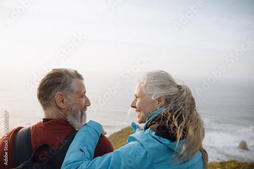 caucasian senior couple sitting on cliff enjoying sunset together looking at each other photo