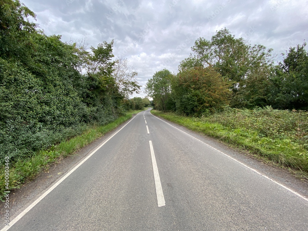 View along, Swine Lane, with trees grass, and heavy clouds in, Ryhill, Wakefield, UK