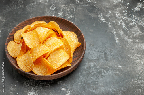 Top view of tasty homemade potato chips on a brown plate on gray background