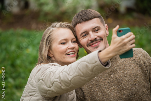 A young husband and wife take a selfie together on a smartphone for a blog on a social network on a green background. Close-up emotions