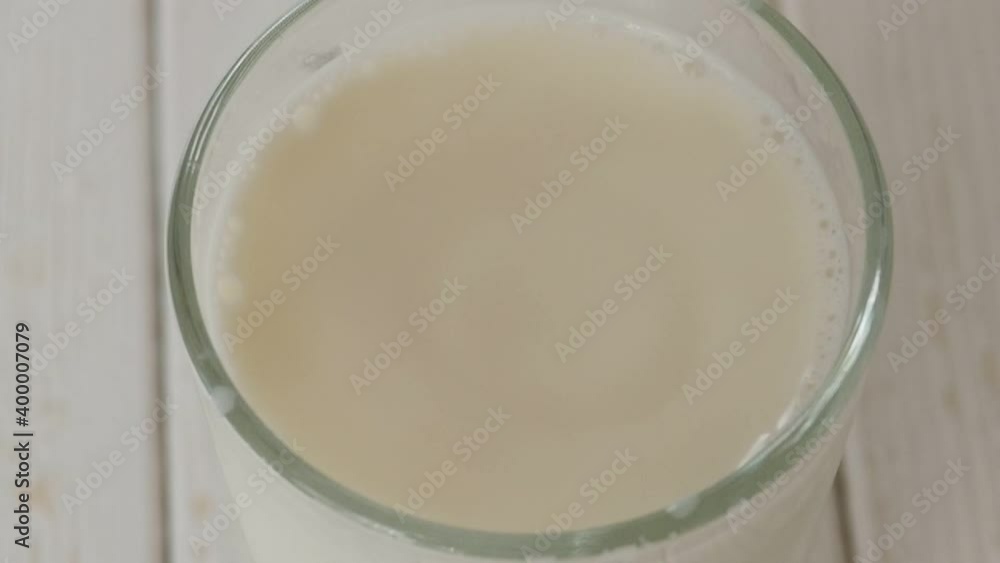 Close-up of milk drops falling into a full glass of milk on a light wooden surface, slow motion. The view from the top. Close-up of milk drops falling into a full glass of milk on a light wooden surface, slow motion. The view from the top.