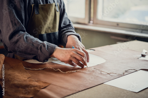 A young guy in a leather workshop transfers a pattern from paper to leather.