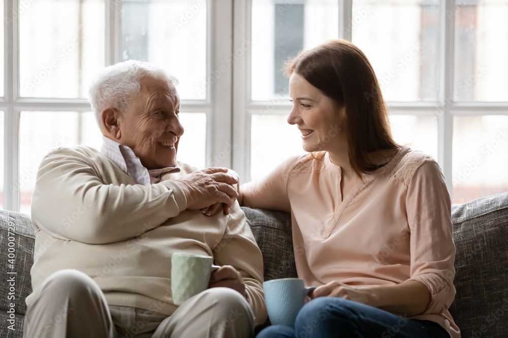 Happy smiling elderly father enjoy conversation with beloved grown daughter discuss news for cup of tea. Caring young woman grandchild come to see mature grandpa having pleasant talk with glad old man Happy smiling elderly father enjoy conversation with beloved grown daughter discuss news for cup of tea. Caring young woman grandchild come to see mature grandpa having pleasant talk with glad old man