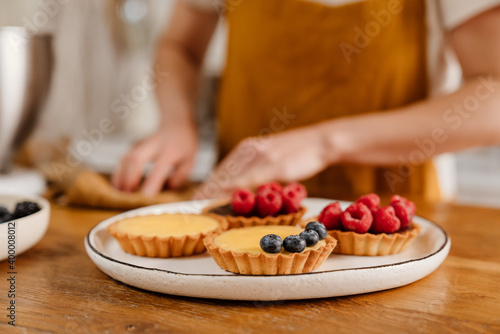 Caucasian pastry chef woman making tarts with berries at cozy kitchen