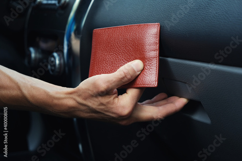Man's hand puts leather wallet in the glove compartment of the car.