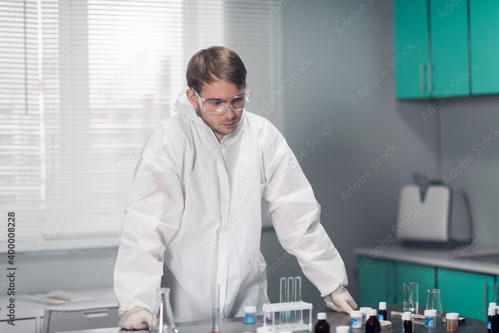 Young pensive chemist leaning on the table in a bright lab.