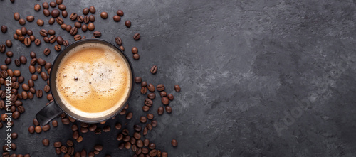 Horizontal banner with cup of coffee and coffee beans on dark stone background. Top view. Copy space