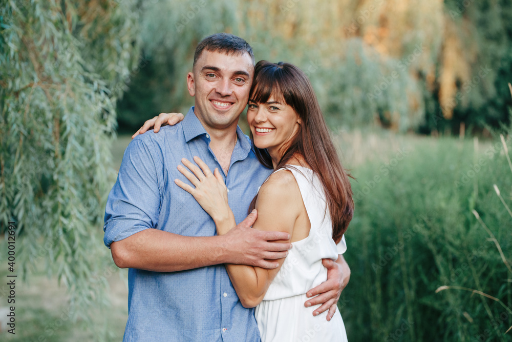 Beautiful smiling couple man woman in love. Husband and wife hugging in park on summer day at sunset. Togetherness and happiness. Authentic real people family outdoors. Beautiful smiling couple man woman in love. Husband and wife hugging in park on summer day at sunset. Togetherness and happiness. Authentic real people family outdoors.
