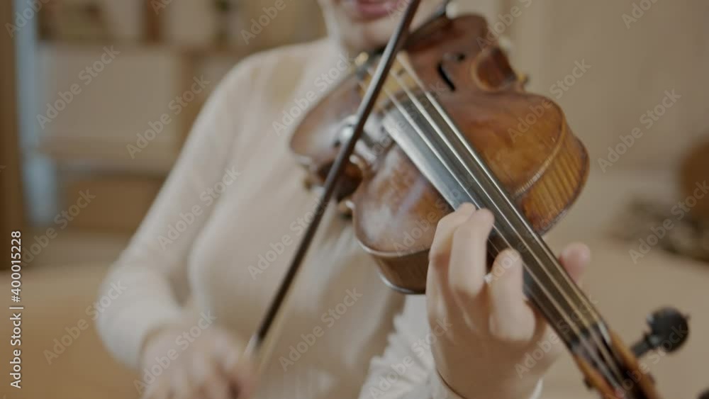 Young woman professional playing violin standing on background of minimalist luxury home interior. Light room with musician woman practicing violin, handheld shot