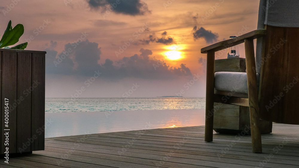 Abenddämmerung mit Sonnenuntergang auf den Malediven im indischen Ozean, mit Lounge-Möbeln auf dem Pool-Deck und traumhafter Aussicht über den Pool aufs Meer