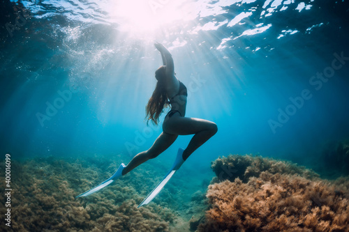 Freediver girl with white fins glides underwater with amazing sun rays and seaweed. Free diving underwater in blue sea