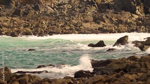Surf coming into a rocky cove in Guernsey on a bright day with messy sea and foam
