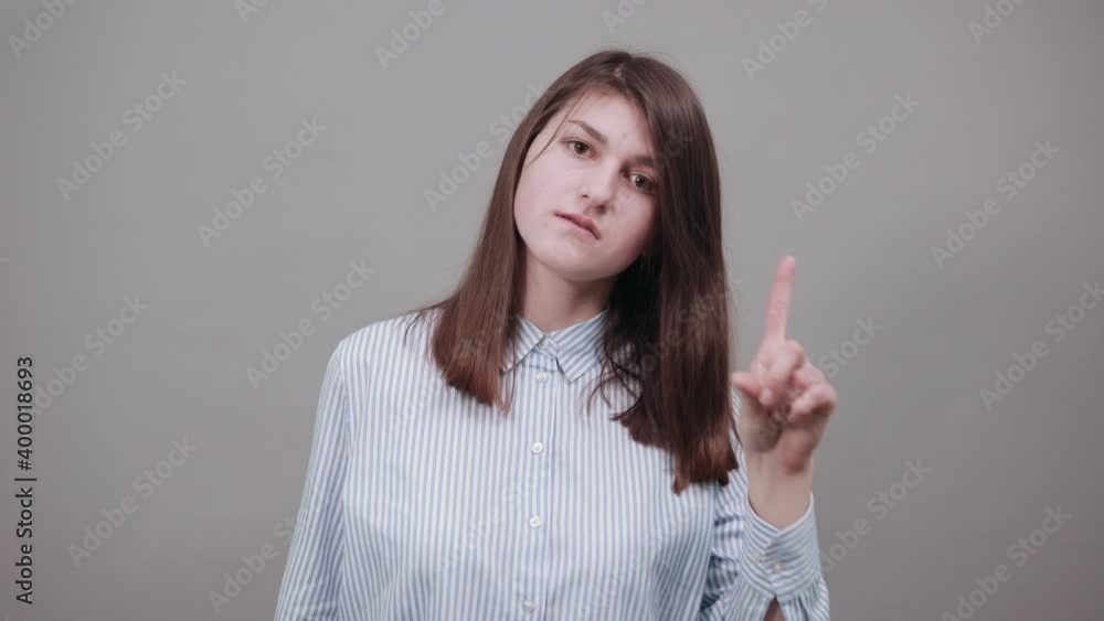 Hand points index finger up, pointing forefinger surprise gift option, great idea. Young attractive woman, dressed blue shirt with brown eyes, brunette hair, grey background Hand points index finger up, pointing forefinger surprise gift option, great idea. Young attractive woman, dressed blue shirt with brown eyes, brunette hair, grey background