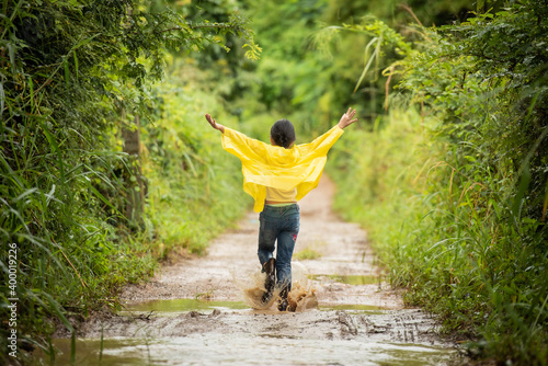 happy little asian  girl running and jumping in puddles after rain in summer. child play in autumn rain. kid playing on the nature outdoors. girl is wearing yellow raincoat and enjoying rainfall..