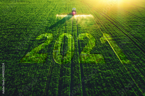 2021 Happy New Year concept and Aerial view of farming tractor plowing and spraying on field.