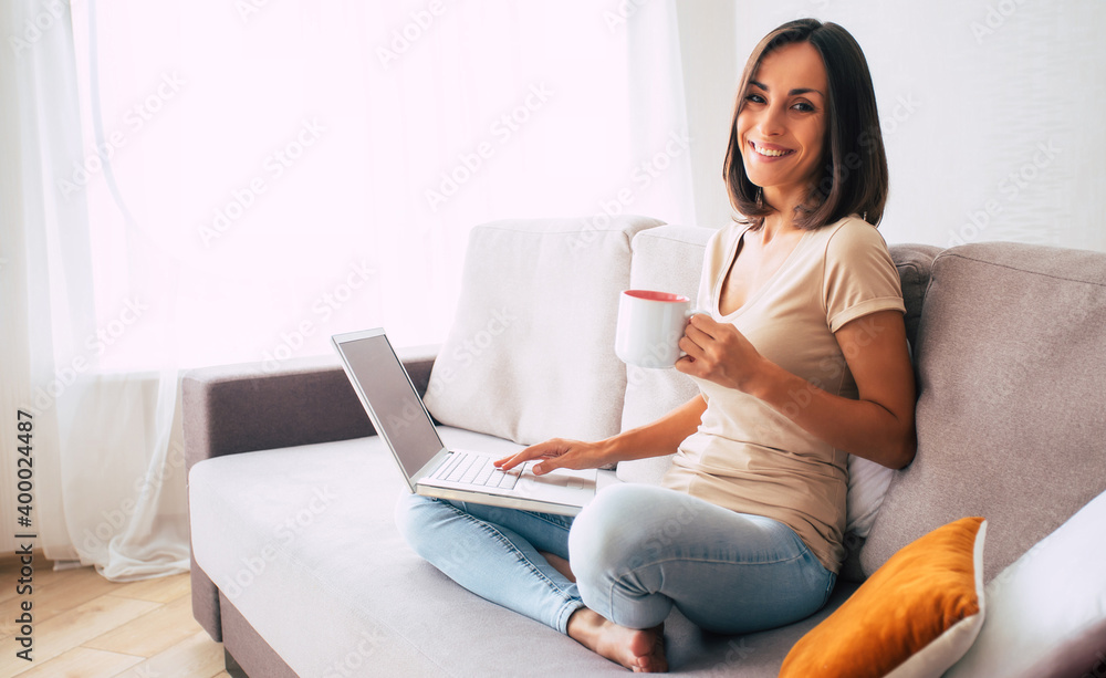 Confident modern cute young woman is online working and relaxing at home on the couch with her laptop on the freelance job Confident modern cute young woman is online working and relaxing at home on the couch with her laptop on the freelance job