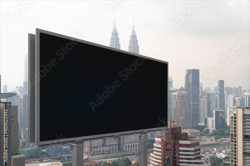 Blank black road billboard with Kuala Lumpur cityscape background at day time. Street advertising poster  mock up  3D rendering. Side view. The concept of marketing communication.