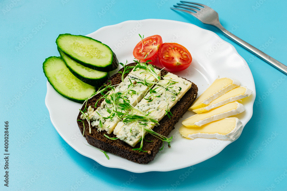 Rye bread with blue cheese and sprouted grains and tomatoes on a plate on a blue background. Rye bread with blue cheese and sprouted grains and tomatoes on a plate on a blue background.