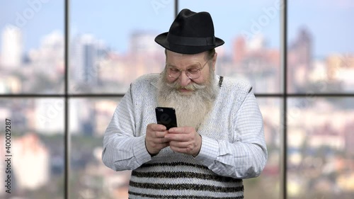 Funny senior man using cell phone. Man with mobile phoe on windows background. photo