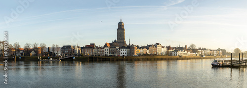 Wide cityscape panorama of the Dutch Hanseatic medieval city of Deventer in The Netherlands seen from the other side of the river IJssel at sunrise with ferryboat quay