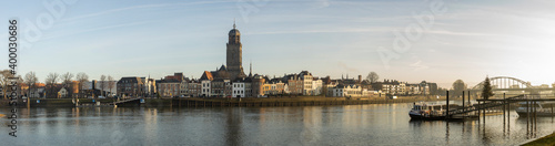 Super wide cityscape panorama of the Dutch Hanseatic medieval city of Deventer in The Netherlands seen from the other side of the river IJssel at sunrise © Maarten Zeehandelaar