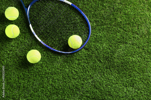 Tennis racket and balls on green grass, flat lay. Space for text