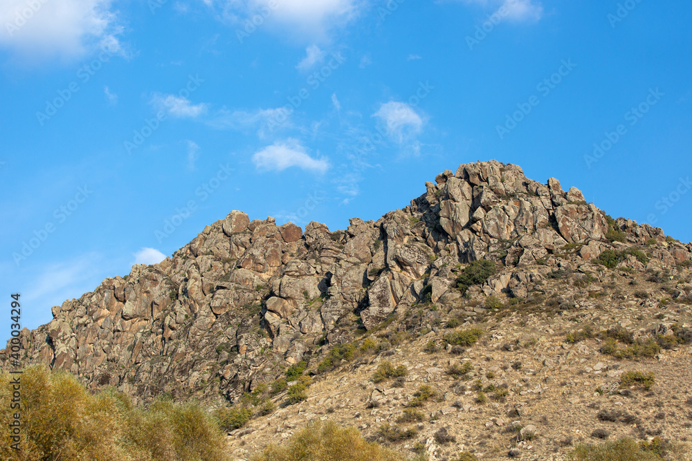 Natural rocky hill in daylight, plants and clear blue sky in the background. Natural rocky hill in daylight, plants and clear blue sky in the background.