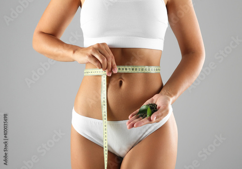 Young woman with measuring tape holding fresh and dry tea leaves on grey background, closeup