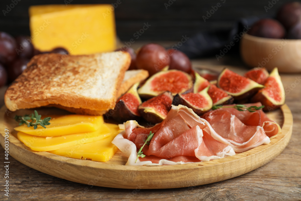 Delicious ripe figs, prosciutto and cheese served on wooden table, closeup