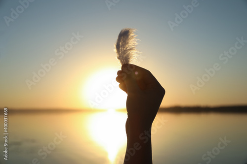 Woman with feather outdoors on sunset, closeup. Healing concept
