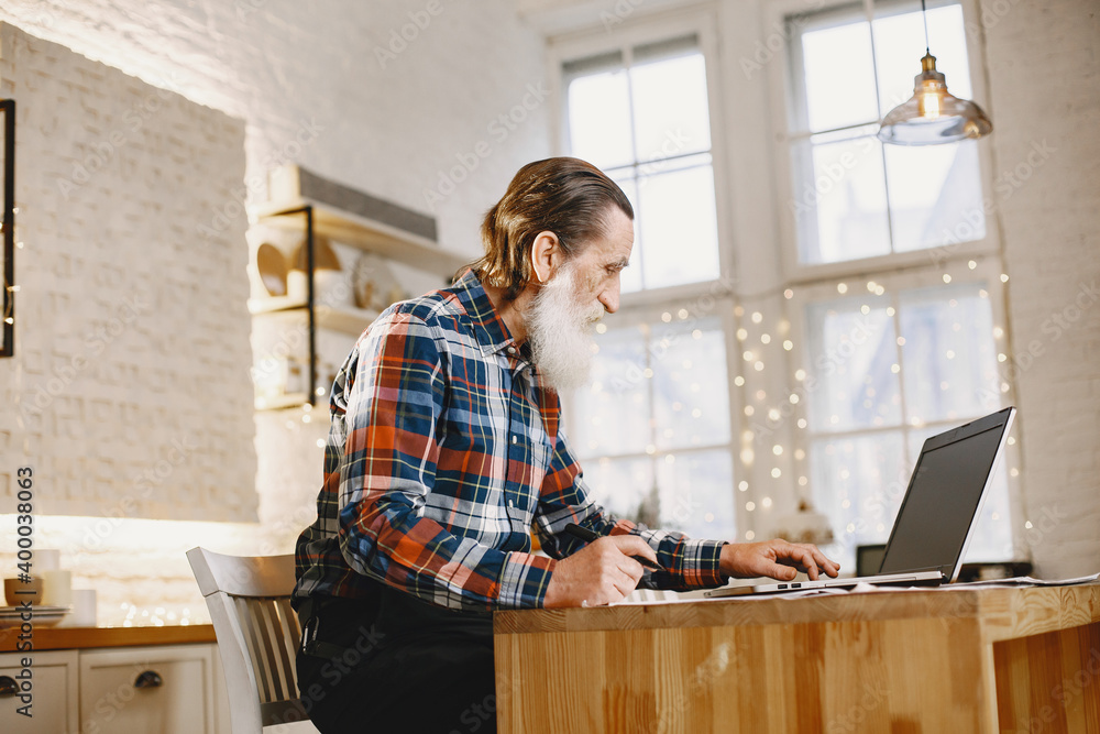 Old man with laptop. Grandfather sitting in a Christmas decorations. Man in a cell shirt. Old man with laptop. Grandfather sitting in a Christmas decorations. Man in a cell shirt.
