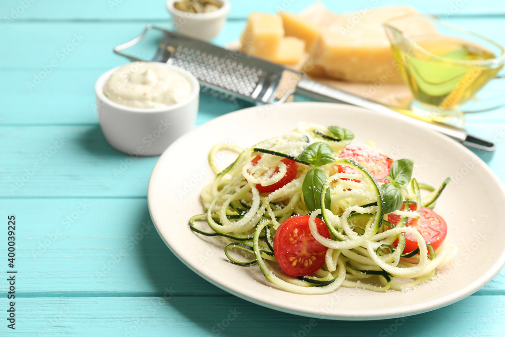 Delicious zucchini pasta with cherry tomatoes, basil and grated cheese served on light blue wooden table Delicious zucchini pasta with cherry tomatoes, basil and grated cheese served on light blue wooden table