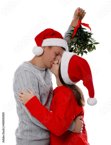 Happy couple kissing under mistletoe bunch on white background