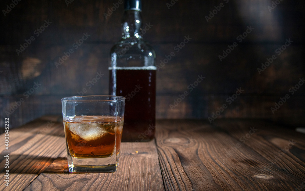 glass of whiskey with ice cubes on rustic wooden table, copy space on dark background glass of whiskey with ice cubes on rustic wooden table, copy space on dark background
