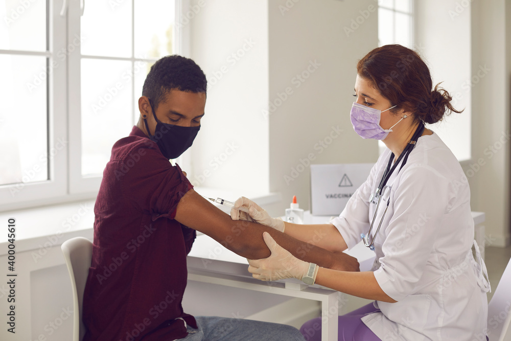 Obraz premium Woman doctor making vaccination with syringe against coronavirus infection for young black man
