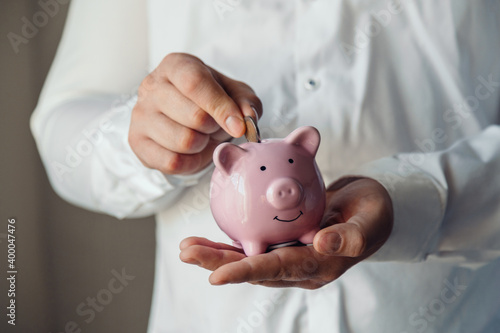 male hands put a coin in a pink piggy bank. The concept of saving money or savings, investment. world crisis