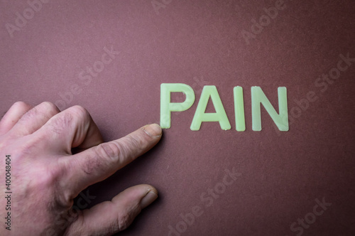 Human fingers pointing the word Pain written with plastic letters on brown paper background, concept