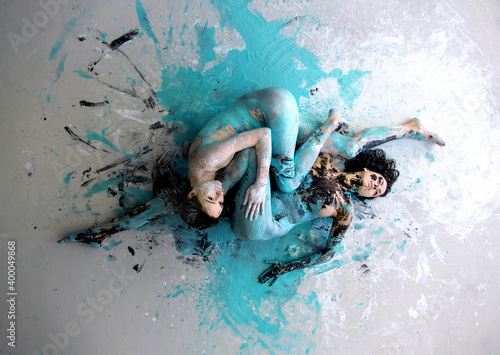 Foto two white black and turquoise abstractly painted sexy young women on the floor, abstract body painting