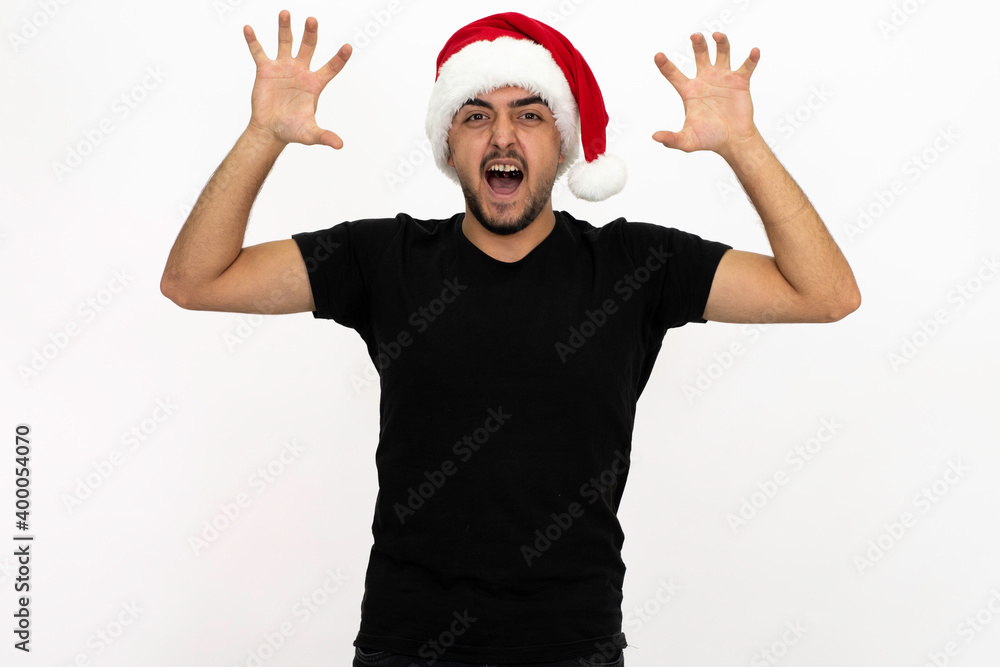Young man wearing a Santa hat. There is a white medical mask. He is wearing a black shirt. Isolated image white background. Young man wearing a Santa hat. There is a white medical mask. He is wearing a black shirt. Isolated image white background.