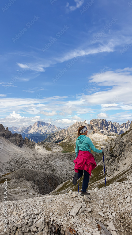 A woman hiking in a high and desolated mountains in Italian Dolomites. The lower parts of the mountains are overgrown with moss and grass. Raw and unspoiled landscape. Clear and sunny day. Solitude