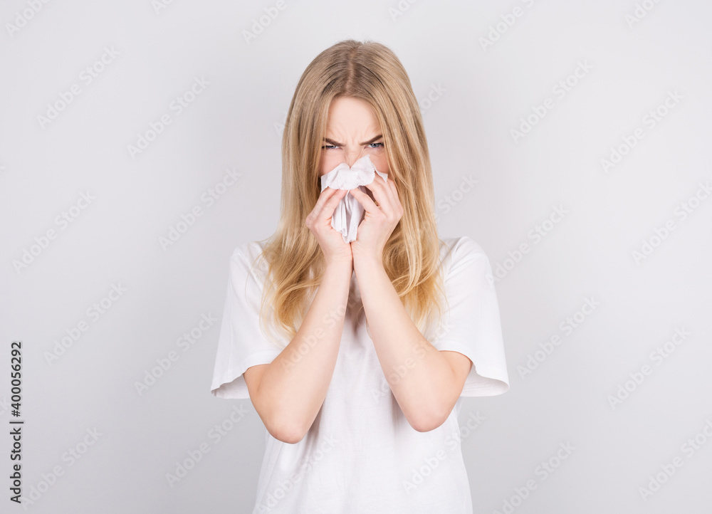 Studio portrait of cute unhealthy caucasian woman with paper napkin sneezing due to allergy, flu or cold Studio portrait of cute unhealthy caucasian woman with paper napkin sneezing due to allergy, flu or cold