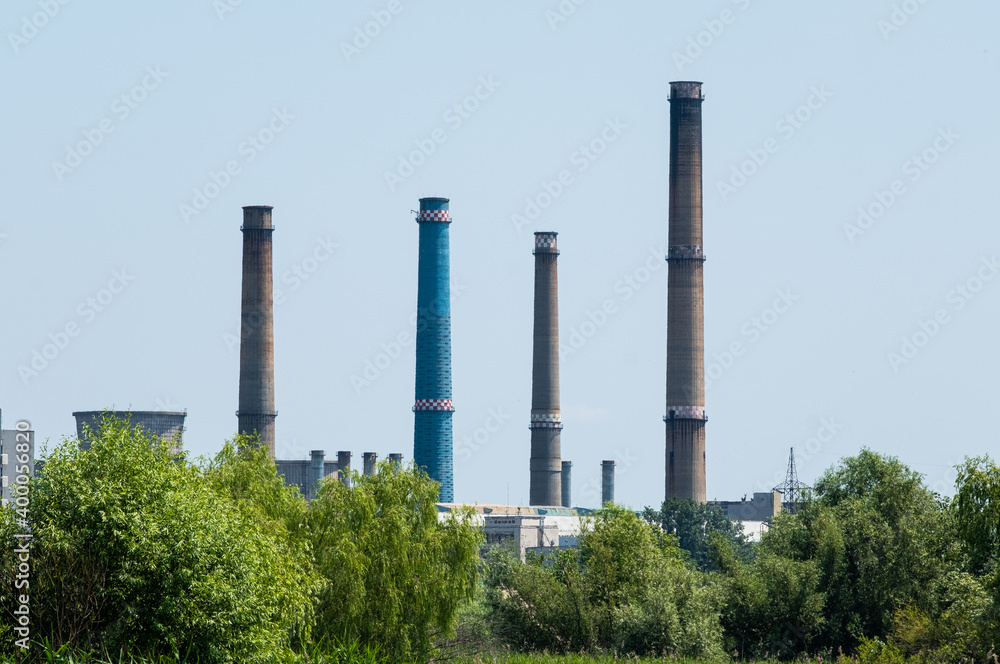 The furnaces of the district heating power plant in Bucharest, seen from the Vacaresti Delta in the middle of the day, among green trees. Delta Vacaresti is a natural park.