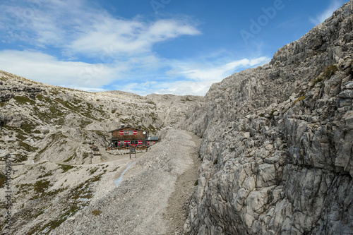 A very narrow and steep pathway, with lots of lose stones in Italian Dolomites. There is a big cottage at the end of it, hidden between the rocks. Raw and unspoiled landscape. Clear and sunny day.