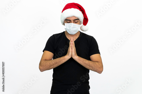 Young man wearing a Santa hat. There is a white medical mask. He is wearing a black shirt. Isolated image white background.